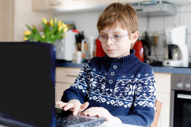 A szemüveges fiú otthon tanul a laptopon az iskolába. Imádnivaló gyerek házi feladatot csinál, jegyzetfüzetet és modern eszközöket használ. Otthoni oktatás koncepciója. - Fotó, kép