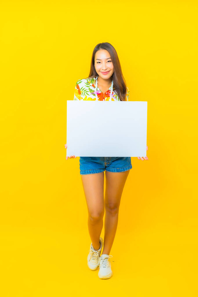Porträt schöne junge asiatische Frau mit weißen leeren Plakatwand auf gelbem Hintergrund - Foto, Bild