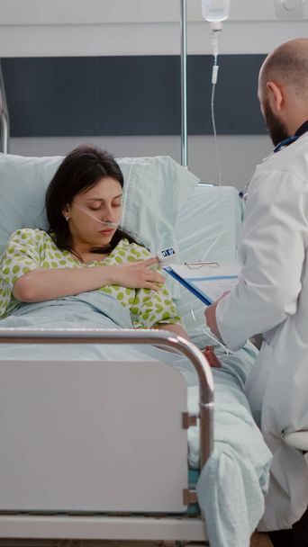 Кавказька самиця з носовою кисневою трубкою сидить у ліжку в лікарні. - Фото, зображення