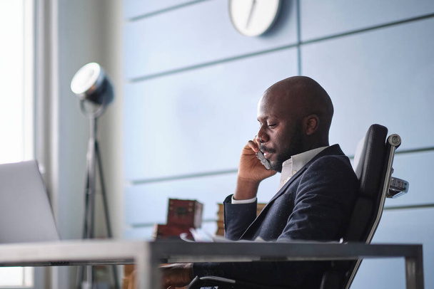 Δύσκολη συζήτηση με πελάτη. Αφροαμερικάνος μιλάει στο τηλέφωνο, ακούει άσχημα απρόσμενα νέα.. - Φωτογραφία, εικόνα