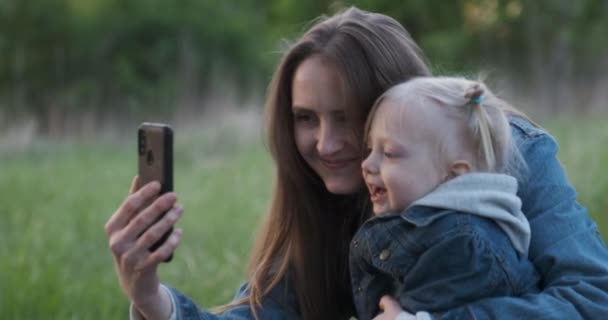 Genç anne küçük kızıyla selfie çekiyor. Parkta çocuklu bir anne kendi fotoğraflarını çekiyor. - Video, Çekim