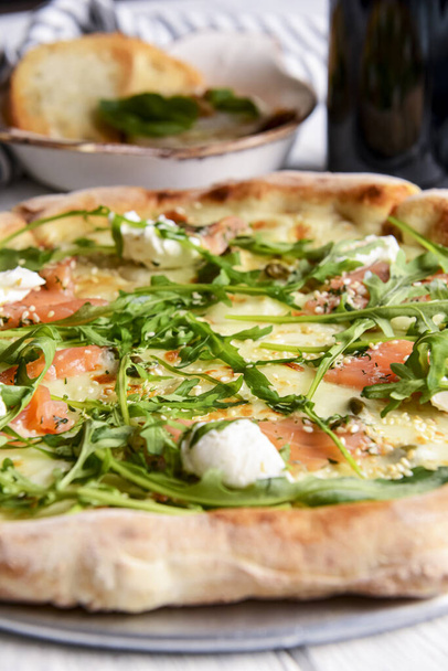 Pizza with mozzarella, salmon slices, fresh arugula. Served with baked cheese camembert and red wine. Italian cuisine concept, traditional pizza recipe. - Фото, зображення