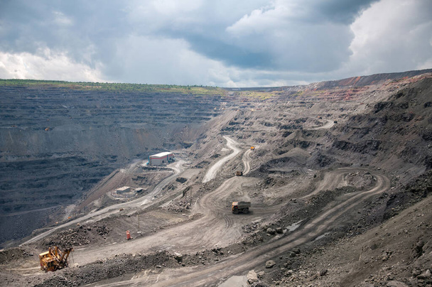 heavy dump trucks, excavators, diggers and locomotives extracting iron ore in deep quarry - Photo, image