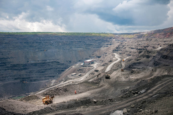 heavy dump trucks, excavators, diggers and locomotives extracting iron ore in deep quarry - Фото, зображення