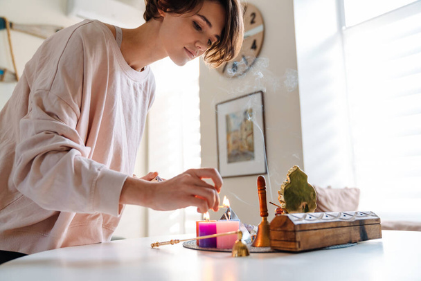 Peaceful beautiful girl lighting candles at home shrine indoors - 写真・画像