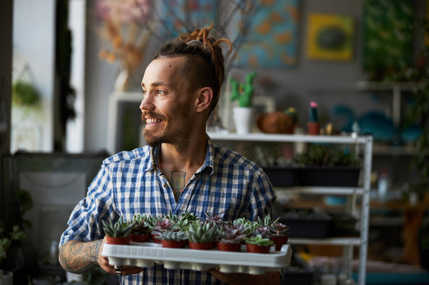 Радісний молодий чоловік з рослинами, що стоять у майстерні
 - Фото, зображення