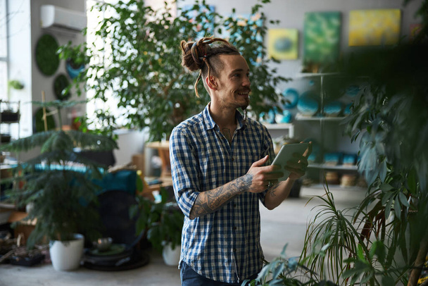 Hombre alegre sosteniendo tableta digital ordenador y las plantas de comprobación - Foto, Imagen