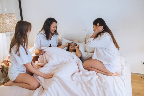 Positieve jonge meisjes vrouwen vrienden binnen op bed op de kip partij thuis. - Foto, afbeelding