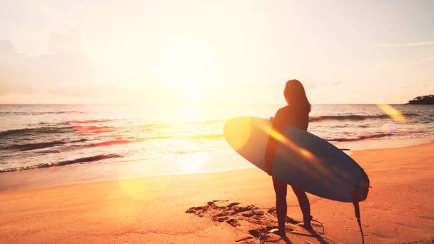 Kadın, tropik günbatımı sahili arka planında sörf tahtası tutuyor. Yaz tatili ve spor macera konsepti. Klasik ton filtre efekti renk biçimi. - Fotoğraf, Görsel