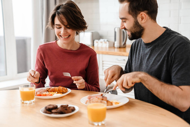 Cheerful attractive young couple having tasty breakfast at the kitchen table - Zdjęcie, obraz
