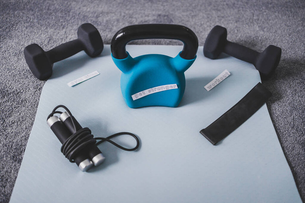 Gym time and exercising in your spare time conceptual image, kettlebell with dumbbells and skipping rop on yoga mat on bedroom floor with Get Stronger message  - Φωτογραφία, εικόνα