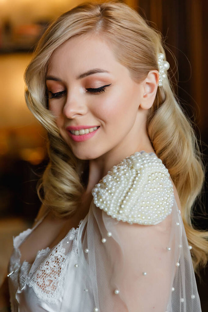 A large portrait of a beautiful blonde and sexy bride with an attractive body, with curls and a pearl hairpin. Looks down. Morning of the bride. - Photo, Image