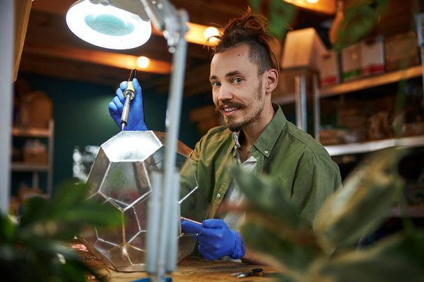 Joyeux jeune homme faisant florarium en verre dans l'atelier - Photo, image