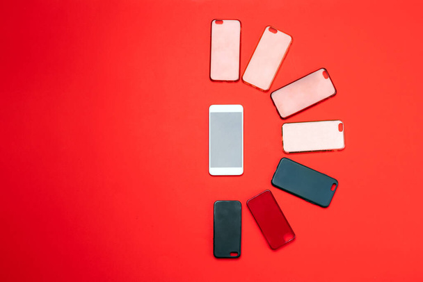 Choice of multicolored plastic back covers for mobile phones on red background with a smart phone on the side - Fotoğraf, Görsel