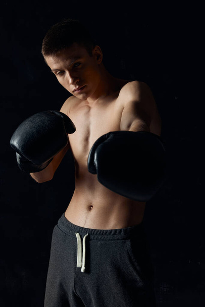 μαύρο φόντο αρσενικό bodybuilder με ένα pump-up κορμό στην προπόνηση γάντια πυγμαχίας - Φωτογραφία, εικόνα