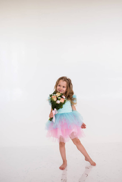 маленькая блондинка в праздничном платье держит букет свежих цветов на белом фоне. С днем рождения! - Фото, изображение