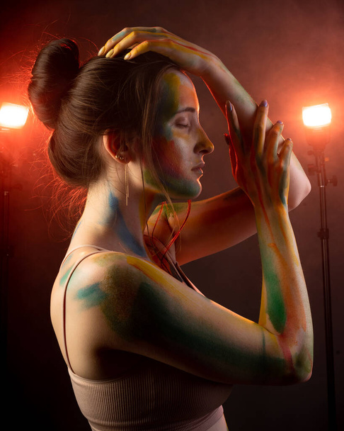 A girl with smears of paint on her face stands in smoke lit by warm light - 写真・画像
