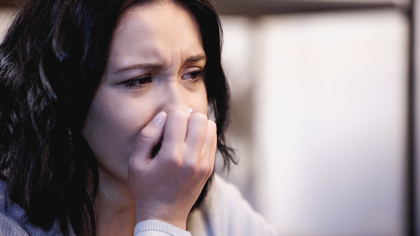 portrait of upset brunette woman crying and covering mouth with hand at home - Photo, Image