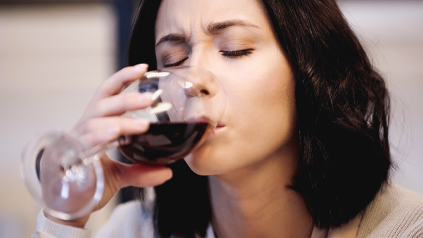 close up άποψη της αναστατωμένης γυναίκας πίνοντας κόκκινο κρασί από γυαλί με κλειστά μάτια στο σπίτι - Φωτογραφία, εικόνα