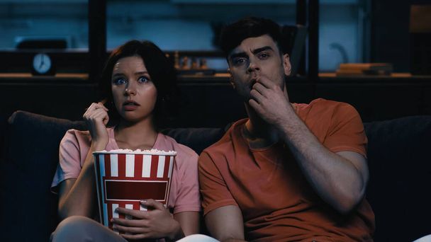 mujer sorprendida sosteniendo cubo con palomitas de maíz y viendo una película con su novio  - Foto, imagen
