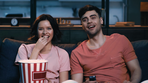 happy woman eating popcorn and watching comedy movie with cheerful boyfriend  - Фото, зображення