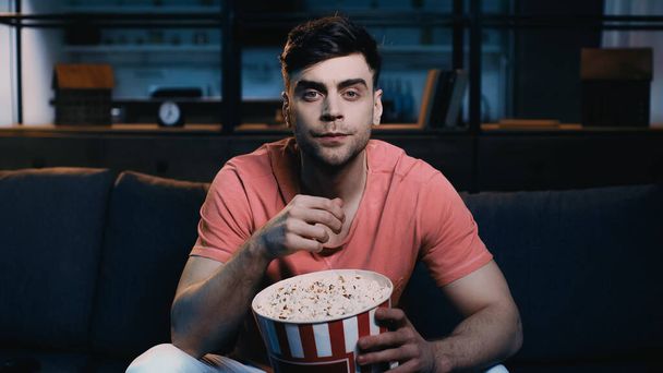 man holding popcorn bucket and watching movie at home  - Foto, Imagen