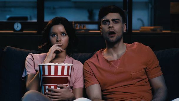 scared woman holding popcorn bucket and watching movie with boyfriend  - Foto, afbeelding