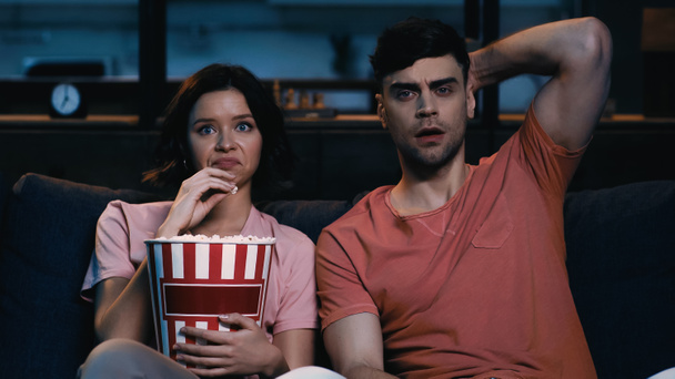 angewiderte Frau hält Popcorn-Eimer in der Hand und schaut Film mit schockiertem Freund  - Foto, Bild