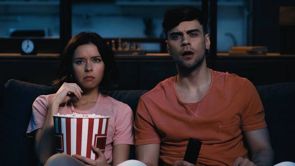 woman eating salty popcorn and watching film with shocked boyfriend  - Foto, immagini