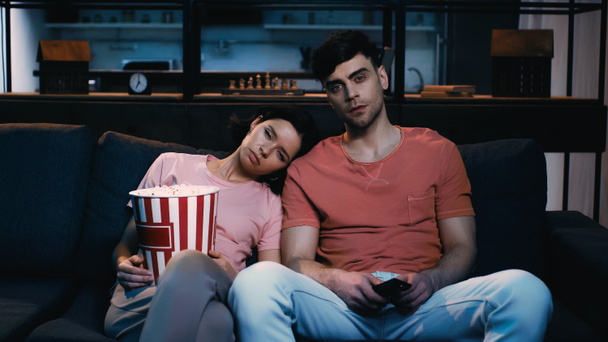 sleepy woman holding popcorn bucket and leaning on shoulder of man while watching movie - Фото, зображення
