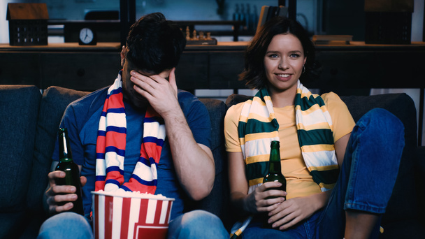 мужчина закрывает лицо рядом с женщиной улыбаясь и смотреть спортивный матч дома - Фото, изображение