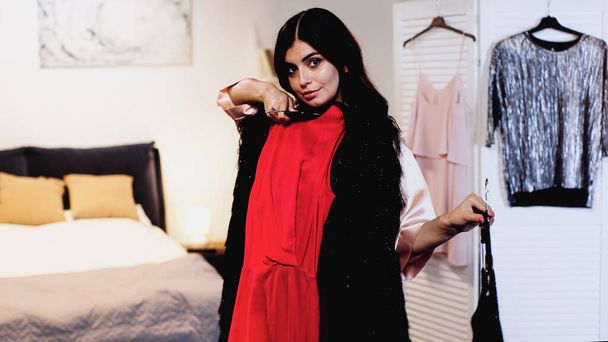 jeune femme en soie rose peignoir essayer des robes sur cintres dans la chambre - Photo, image