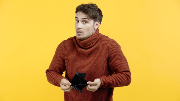 Μπερδεμένος άντρας που κρατάει άδειο πορτοφόλι και κοιτάζει την κάμερα απομονωμένη στο κίτρινο  - Φωτογραφία, εικόνα