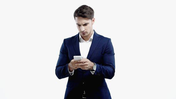 Joven gerente en traje usando teléfono celular aislado en blanco  - Foto, imagen
