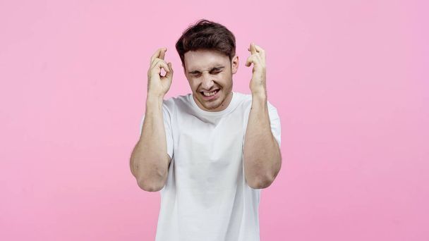 Smiling man with closed eyes showing crossed fingers isolated on pink - Fotografie, Obrázek