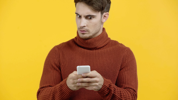 Беспокойный мужчина в свитере с помощью смартфона изолирован на желтый  - Фото, изображение