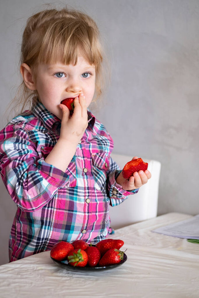 Beautiful little one eating big strawberries with two hands - Fotó, kép