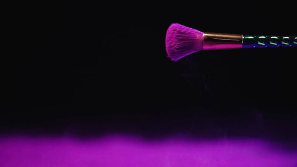 cosmetic brush with purple holi paint on black background  - Foto, afbeelding
