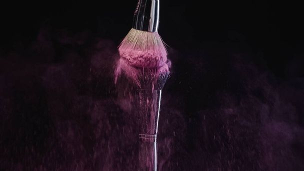 cosmetic brushes hitting and making splashes of colorful purple holi paint on black background - Photo, image