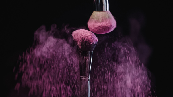pinceles cosméticos haciendo salpicaduras de pintura holi púrpura sobre fondo negro - Foto, imagen