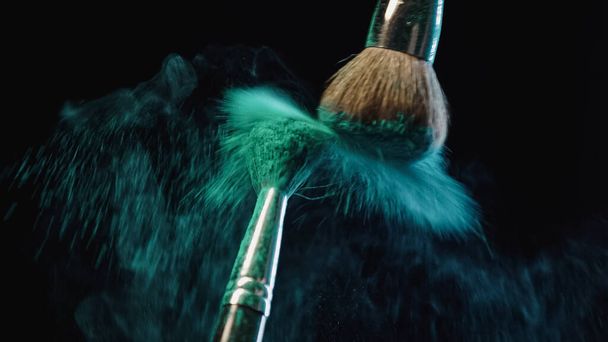 Kozmetik fırçalar siyah arkaplanda mavi toz damlaları oluşturuyor - Fotoğraf, Görsel