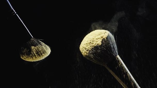 cosmetic brushes with yellow holi powder on black background - Photo, Image