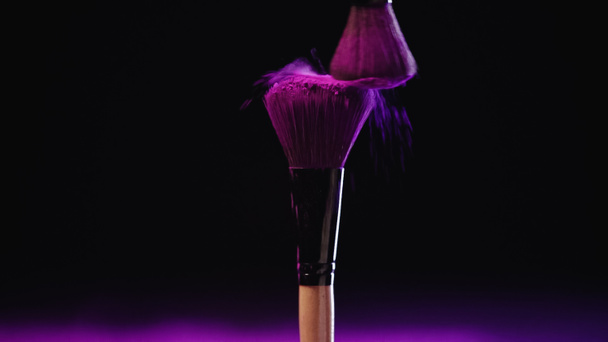 cosmetic brushes with pink powder of holi paint hitting and splashing on black background - Foto, imagen