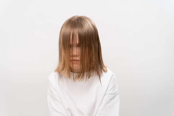 Ein trauriges kleines Mädchen mit Haaren bedeckt das Gesicht auf weißem Hintergrund. Kinderfrisuren und Haarkosmetik. Leichtes Bürsten. Psychologische Hilfe für Kinder. - Foto, Bild