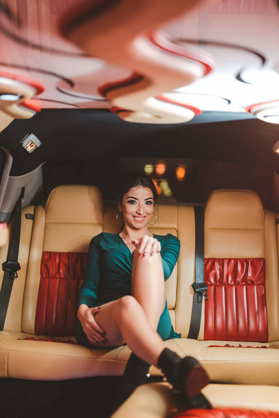 A pretty Caucasian lady with a green evening dress posing while sitting in a luxury limousine - Φωτογραφία, εικόνα
