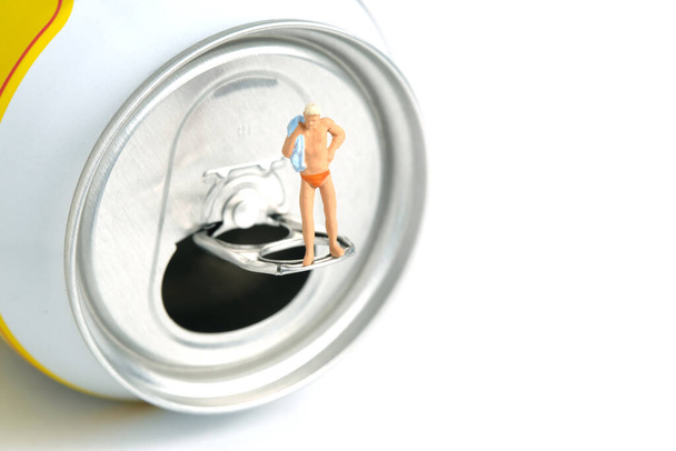 Miniature people toy figure photography. Creative summer vacation concept. A men standing above soft drink canned getting ready to swim. Image photo - Photo, Image