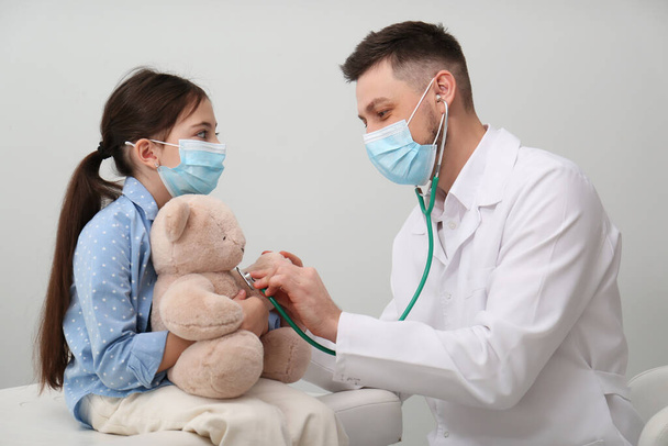 Pediatrician playing with little girl during visit in hospital. Doctor and patient wearing protective masks - Foto, imagen