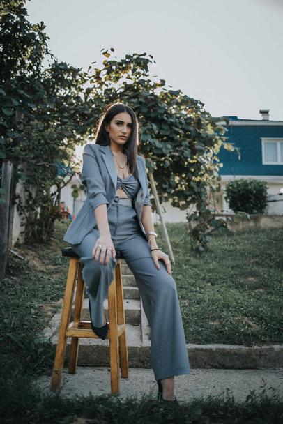 A Caucasian lady wearing a gray crop top and blazer and posing white sitting on a wooden chair - Φωτογραφία, εικόνα
