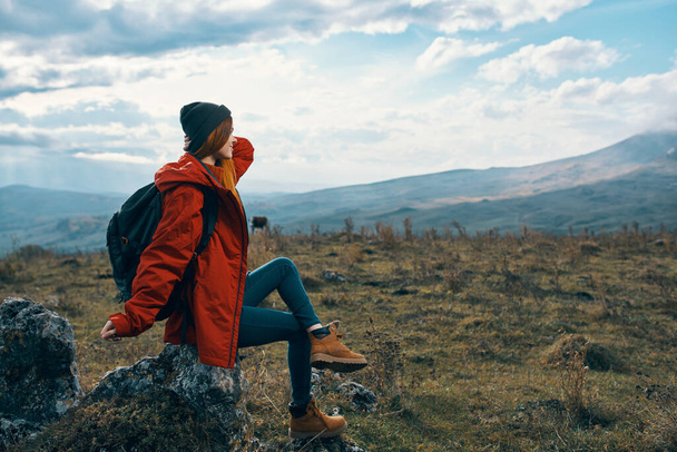 Matkustaja punaisessa takissa istuu kivellä vuorilla luonnossa. Laadukas kuva - Valokuva, kuva