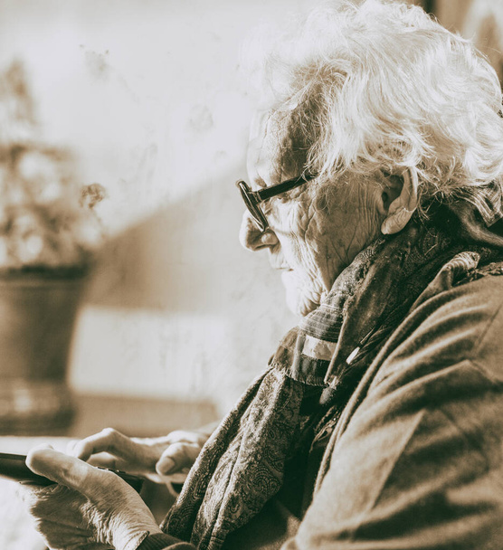 Donna anziana con gli occhiali guardando il telefono cellulare a casa
. - Foto, immagini